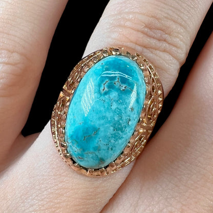 A yellow gold filigree style ring mounted with an oval Pilot Mountain turquoise stone.