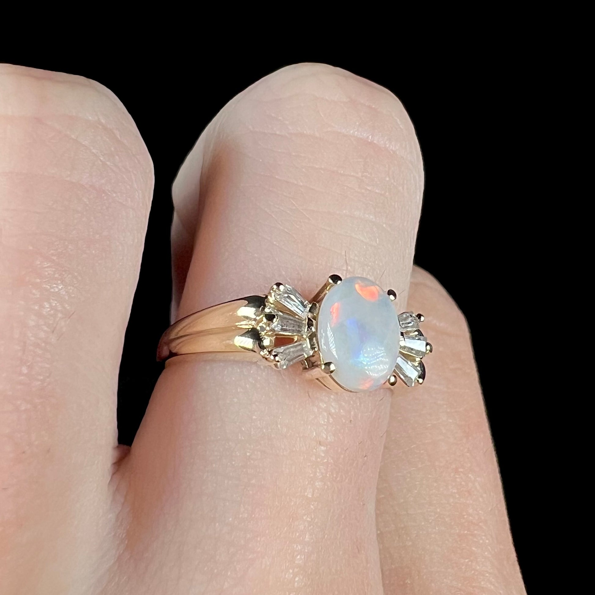 A yellow gold ring set with a natural Australian opal and tapered baguette cut cubic zirconia accents.