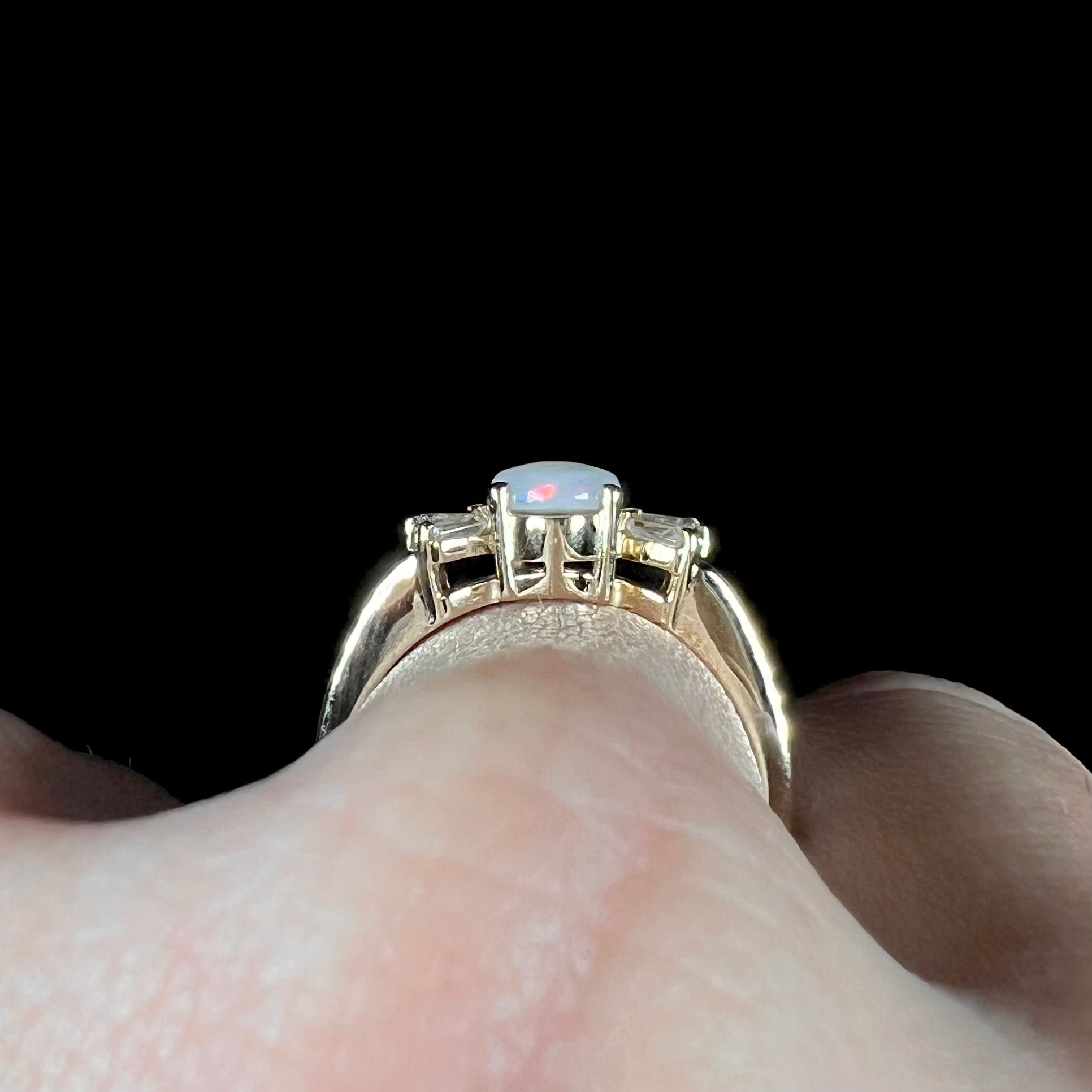 A yellow gold ring set with a natural Australian opal and tapered baguette cut cubic zirconia accents.