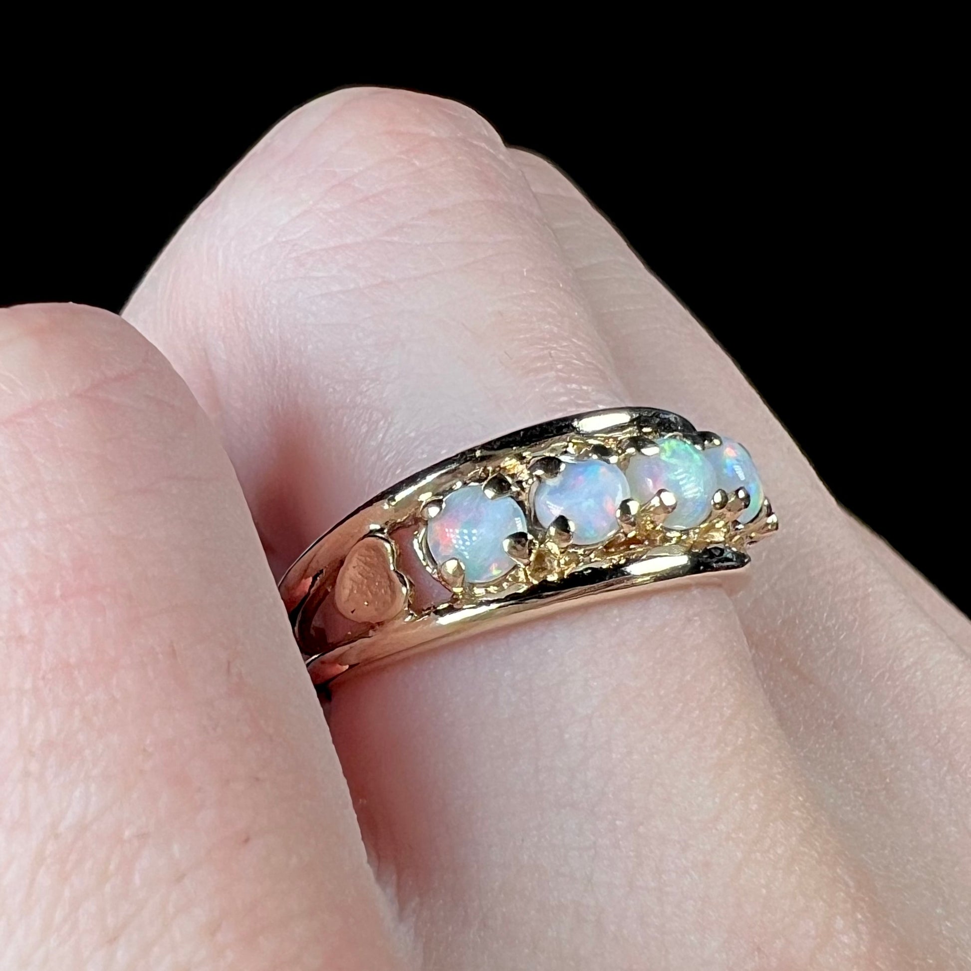 A yellow gold band set with five round cabochon cut opals and heart design accents.