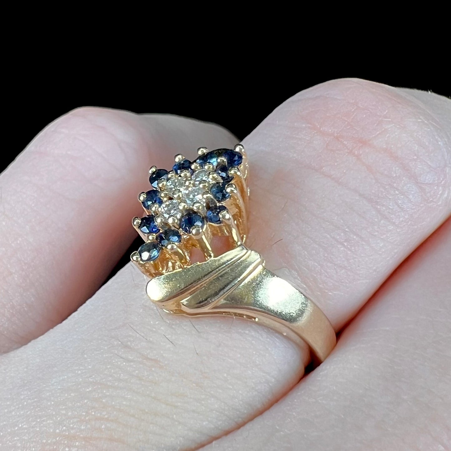 An estate, yellow gold ladies' cluster ring mounted with four round diamonds and twelve round blue sapphires.