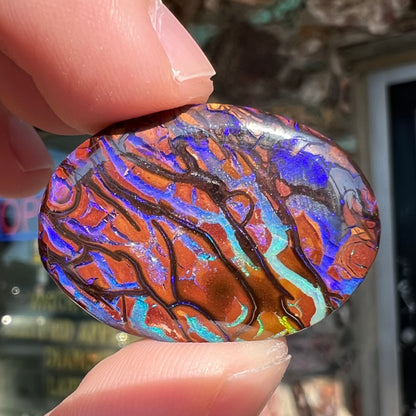 A loose, oval cabochon cut boulder opal from Koroit, Australia.  The opal has violet and purple veins.