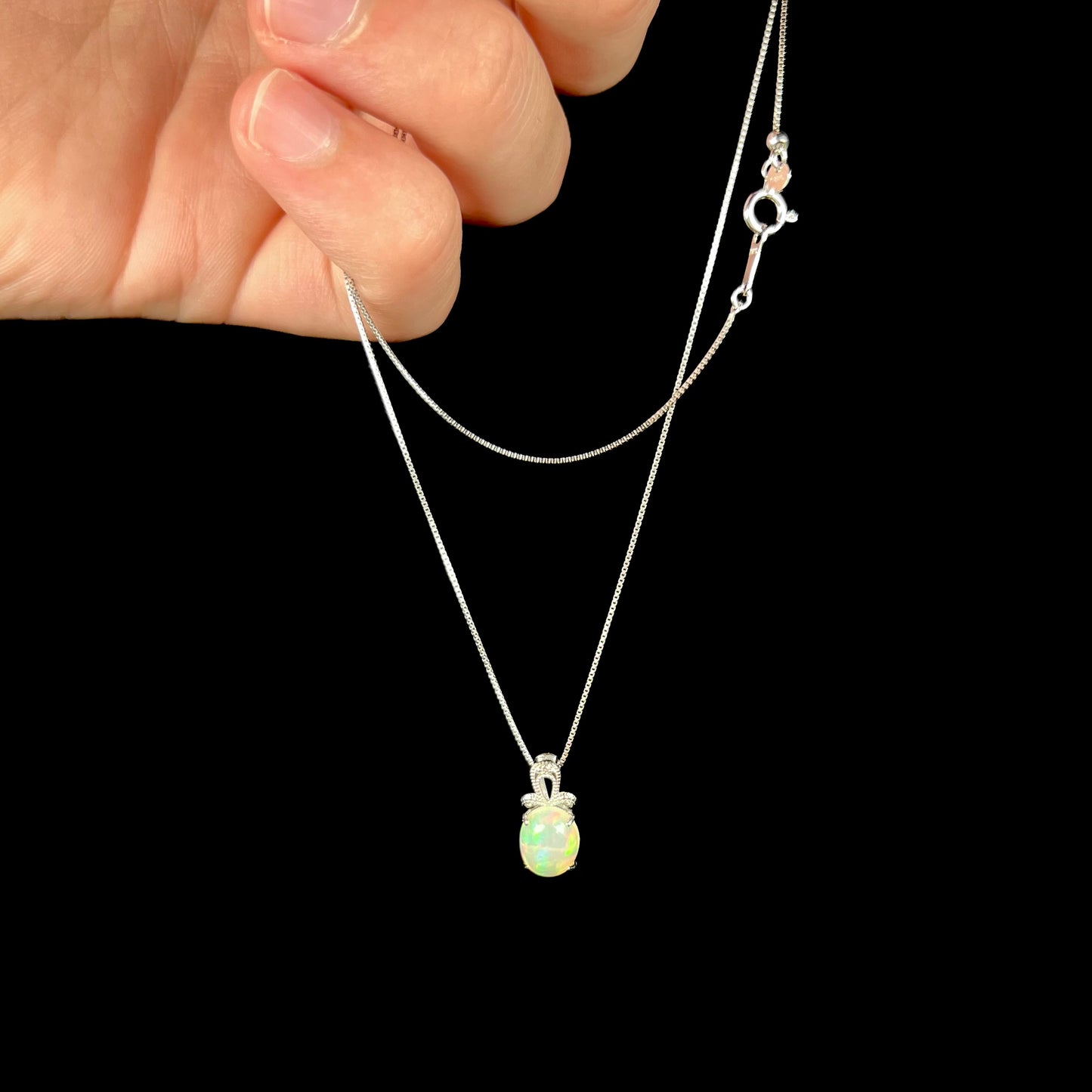 An oval cut Ethiopian opal mounted in a diamond-accented, 18 karat white gold pendant on a box chain.