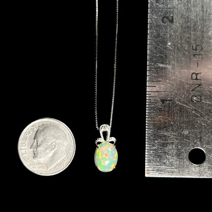 An oval cut Ethiopian opal mounted in a diamond-accented, 18 karat white gold pendant on a box chain.