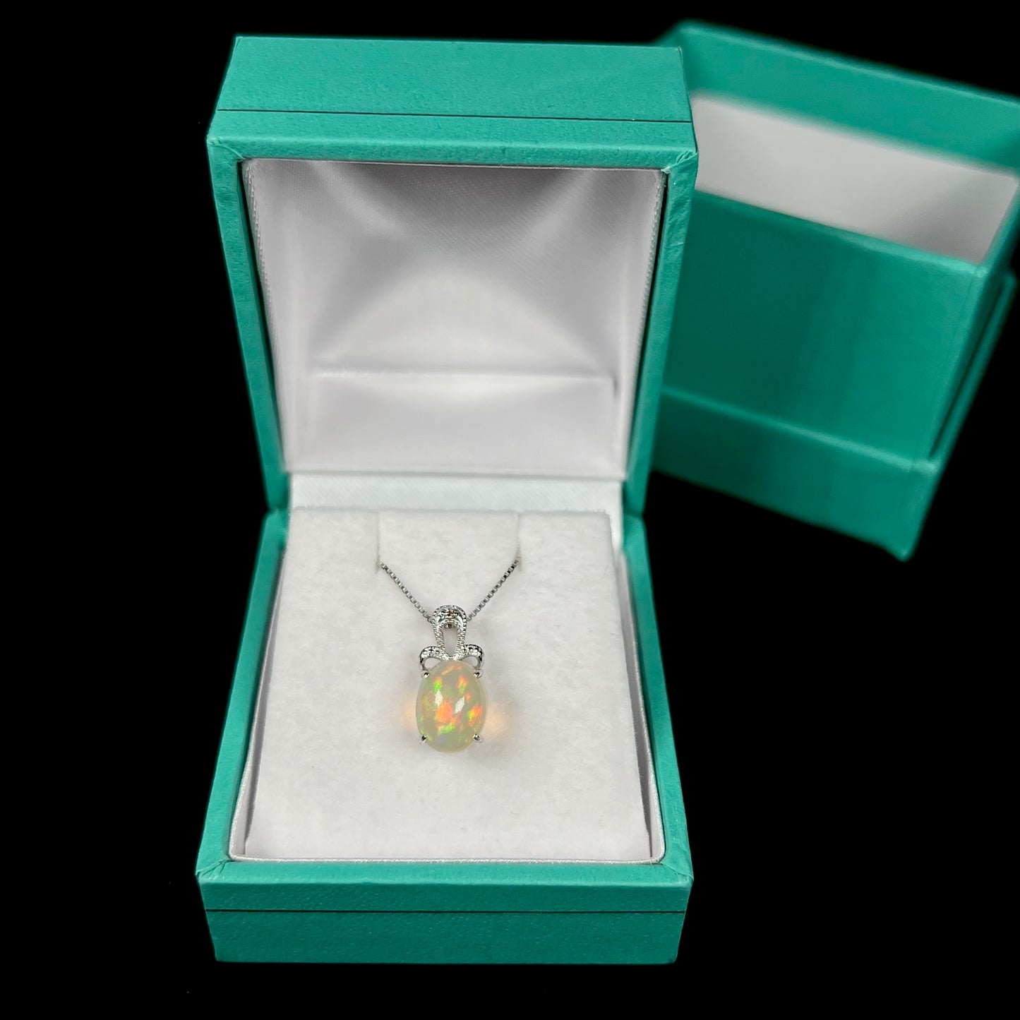 An oval cut Ethiopian opal mounted in a diamond-accented, 18 karat white gold pendant on a box chain.