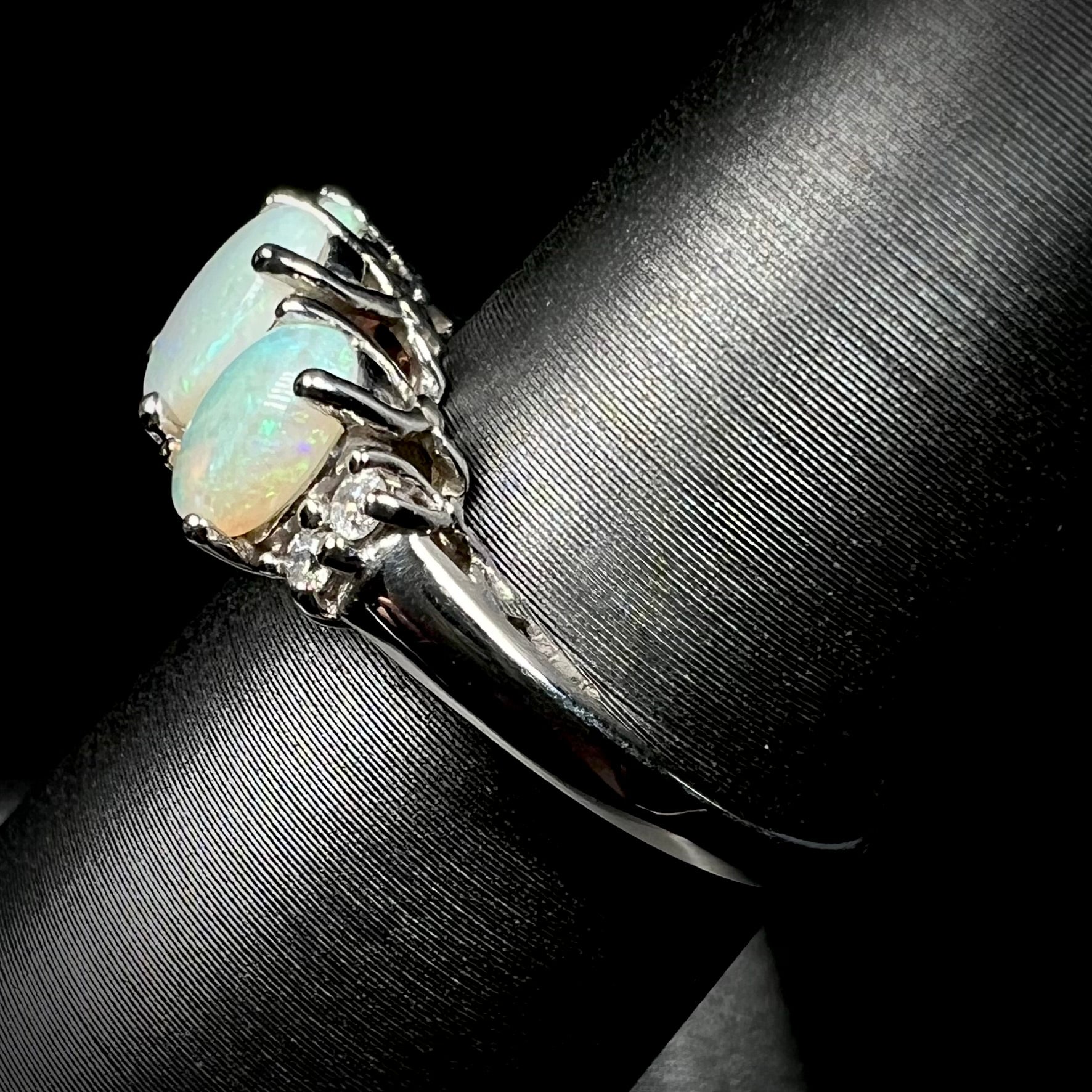 A ladies' white gold ring prong-set with three natural white opals and diamond accents.  The opals play a green color.