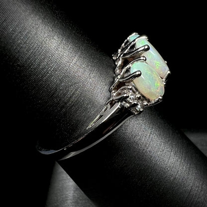 A ladies' white gold ring prong-set with three natural white opals and diamond accents.  The opals play a green color.