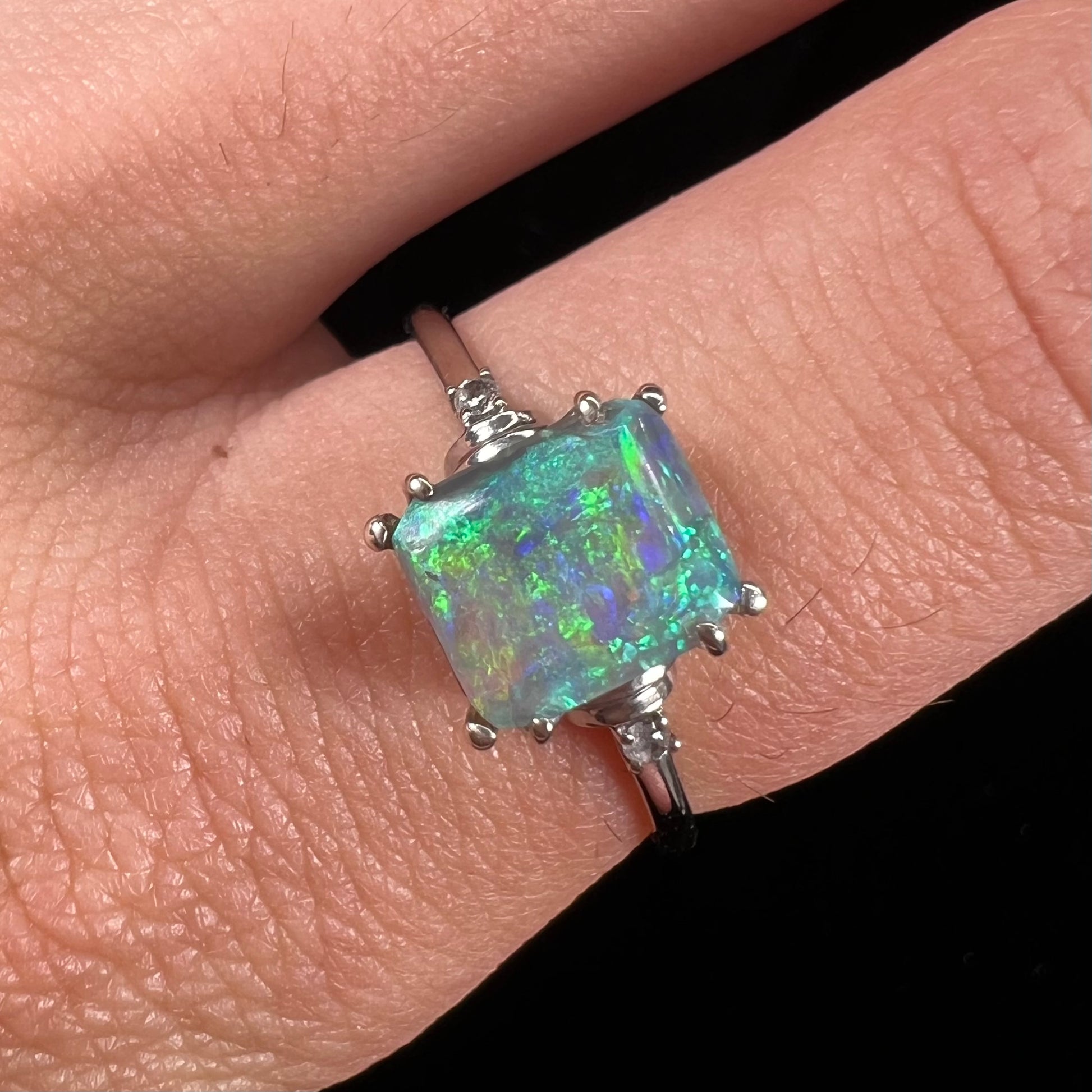 A ladies' white gold ring set with a rectangle cut black opal stone with round white sapphire accent stones.