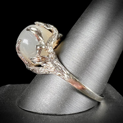 A ladies' organic style white gold moonstone ring.  The moonstone shows white adularescence on a creamy white body color.  Prongs resemble leaves holding the stone.