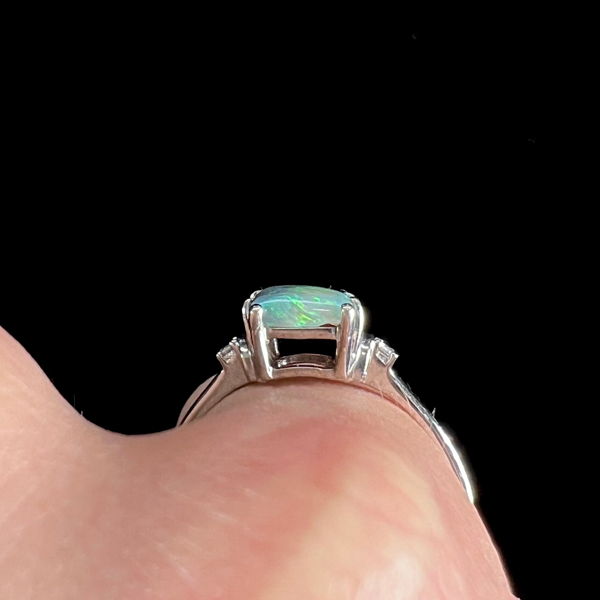 A ladies' white gold ring set with a rectangle cut black opal stone with round white sapphire accent stones.