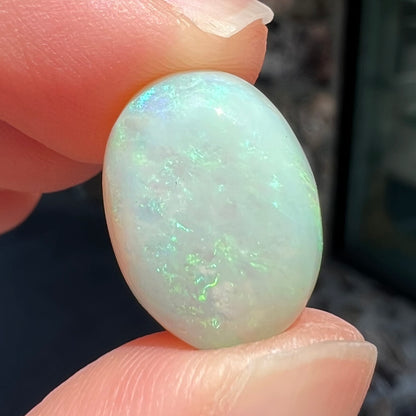 An oval cabochon cut white opal stone from Coober Pedy, Australia.  The opal has subtle colors of green and blue.