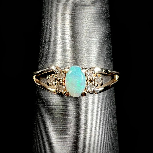A ladies' yellow gold opal and diamond pinkie ring.  The ring is a small size, and the opal shines green and blue colors.