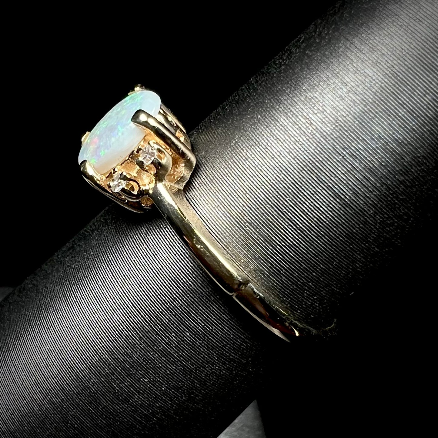 A dainty yellow gold ring set with a Coober Pedy opal with green flashfire pattern and diamond accents.