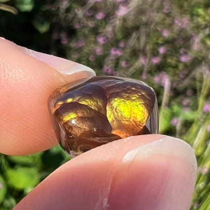 A loose, round Mexican fire agate stone.  The stone shines colors of green, yellow, and orange.