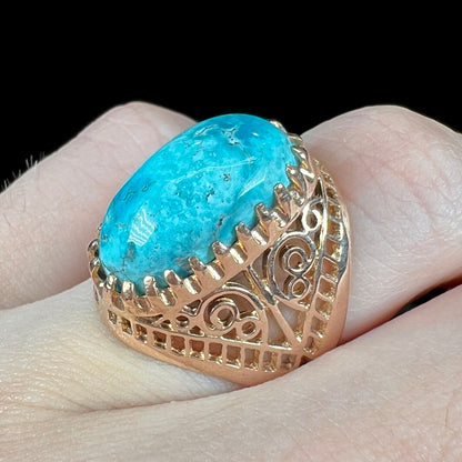 A yellow gold filigree style ring mounted with an oval Pilot Mountain turquoise stone.