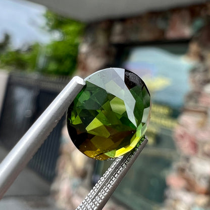 A loose, round checkerboard cut green tourmaline stone with flashes of yellow.