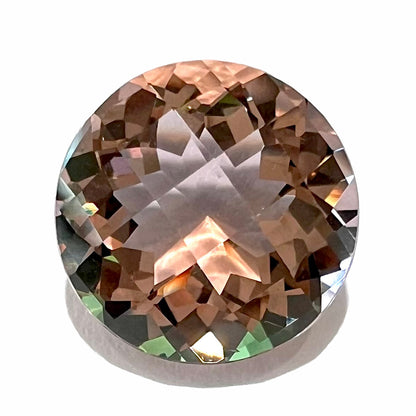 A loose, round brilliant checkerboard cut Zandrite gemstone.  The stone changes colors from greenish tan to purple.