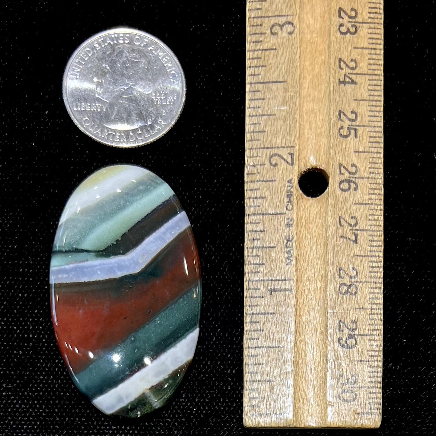 Loose Arizona agate cabochon for sale set on white background.  Stone is striped with red, green, and white.