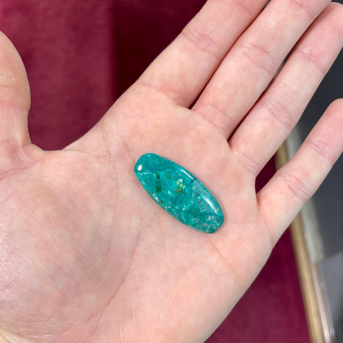 A loose, oval cabochon cut chrysocolla stone with blue azurite inclusions.