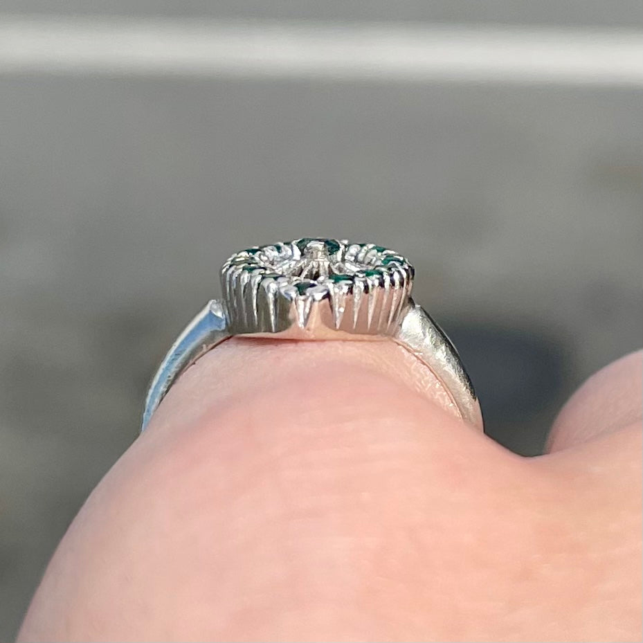 A vintage marquise shape white gold ring set with a halo of round cut emeralds around a single center stone.