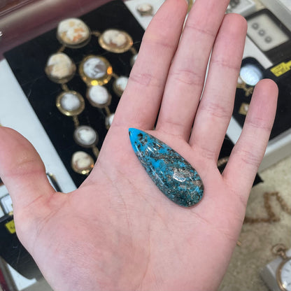 A loose, teardrop shaped, cabochon cut turquoise stone from Kingman, Arizona.  Pyrite inclusions can be seen.