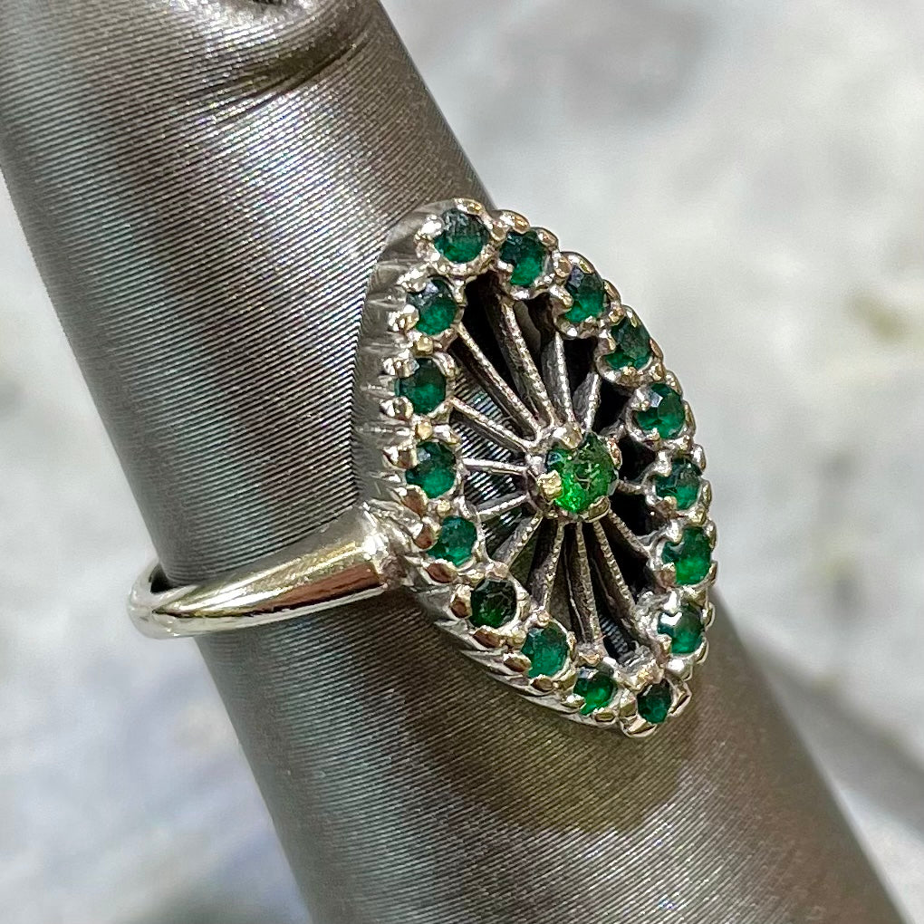 A vintage marquise shape white gold ring set with a halo of round cut emeralds around a single center stone.