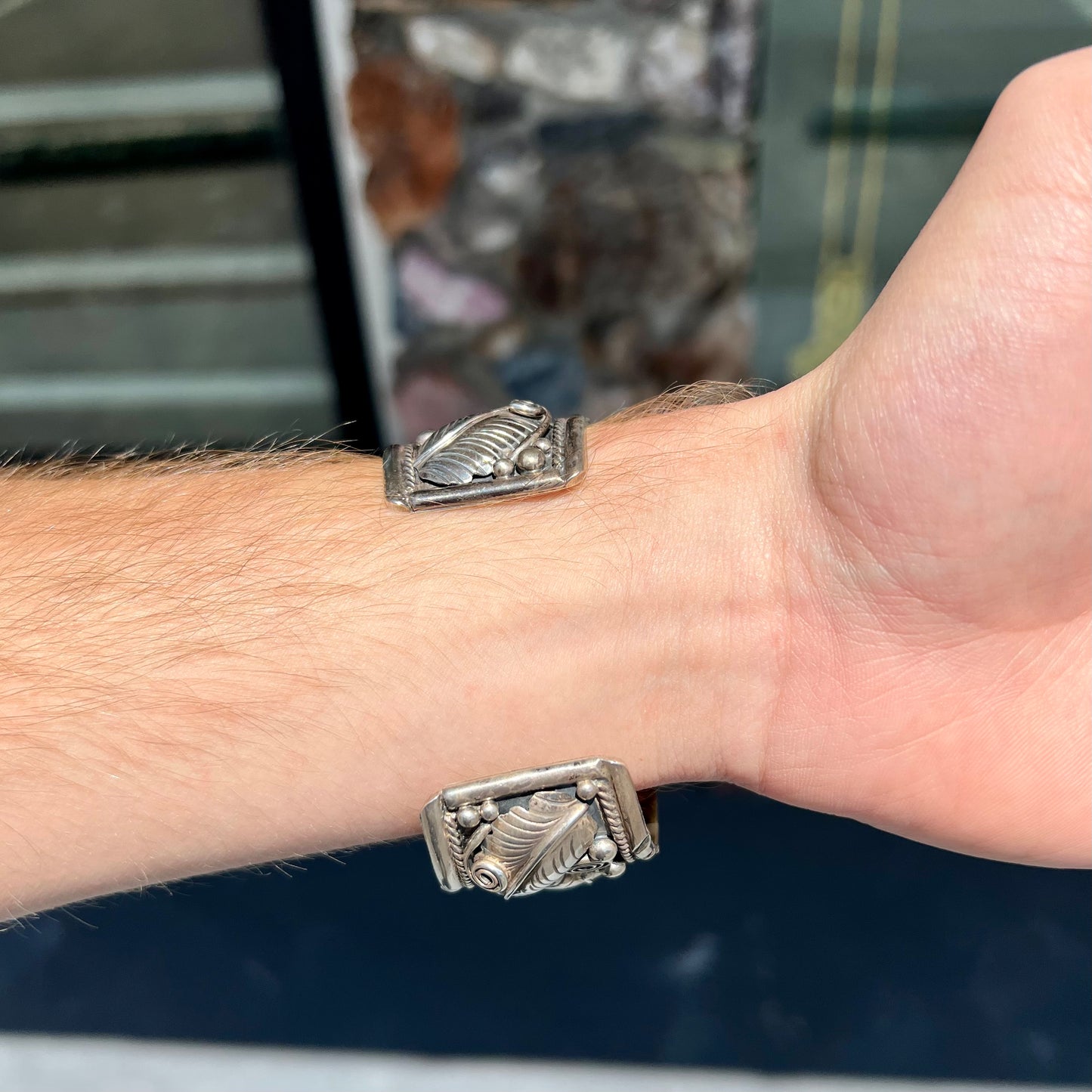 An ornate men's sterling silver turquoise cuff bracelet.  There are three turquoise stones set with silver feathers.