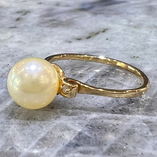 A simple, vintage, yellow gold pearl ring set with two side diamonds.