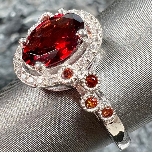 A silver garnet and CZ halo ring.  The center stone is a red almandine garnet, and the side garnets are orange.