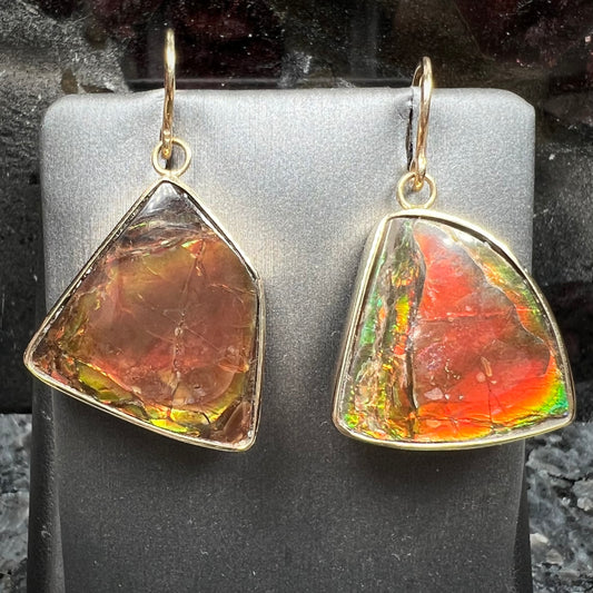 Yellow gold French wire dangle earrings bezel set with two polished freeform cut red ammolite fossils.