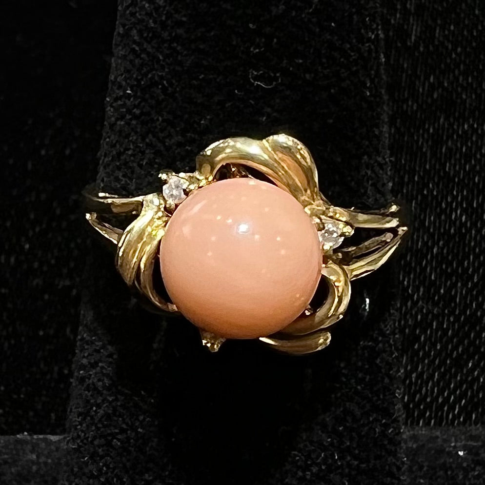 A vintage split shank flower ring set with a round pink coral sphere and diamond accents.