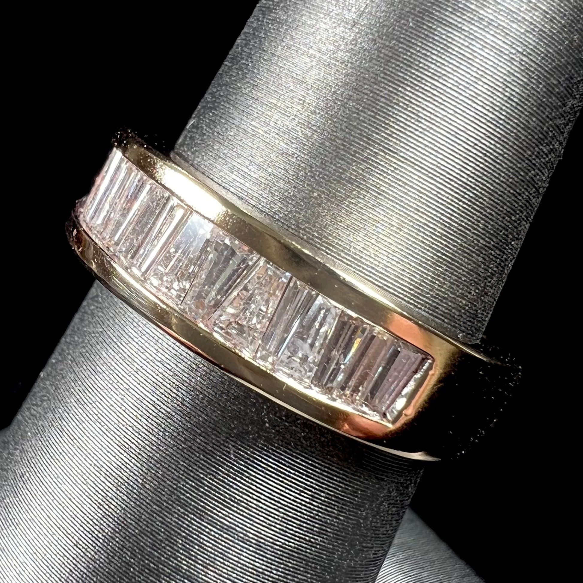 A ladies' yellow gold ring channel set with a row of baguette cut diamonds.