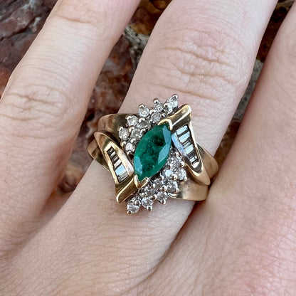 A yellow gold marquise cut emerald and diamond ring.  The diamonds are prong set round cuts and channel set baguette cuts.