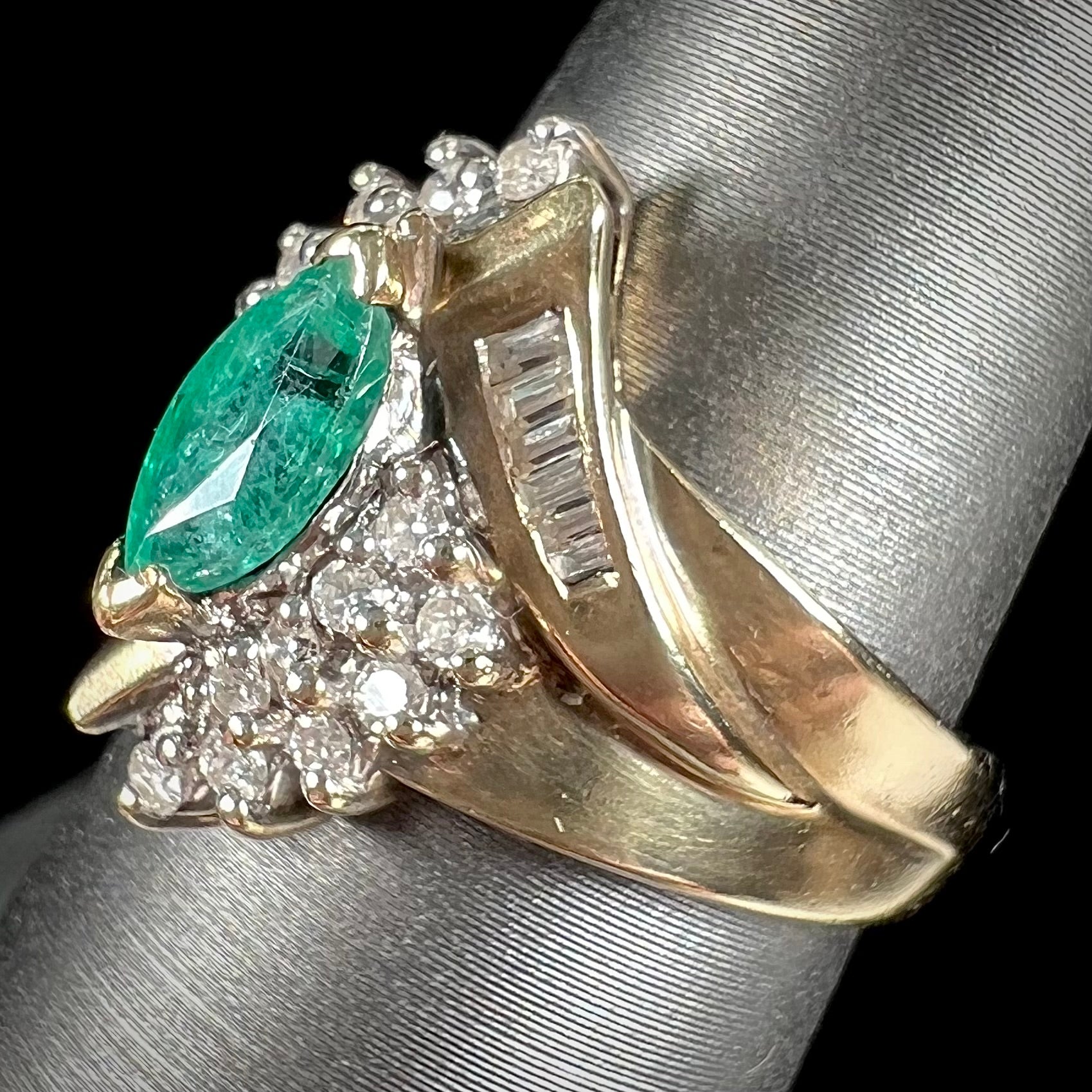 A yellow gold marquise cut emerald and diamond ring.  The diamonds are prong set round cuts and channel set baguette cuts.