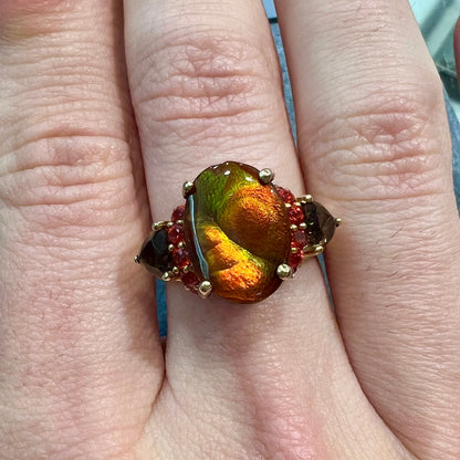 A ladies yellow gold fire agate ring set with trillion cut smoky quartz and round cut red-orange garnet accents.  The fire agate displays green and red.