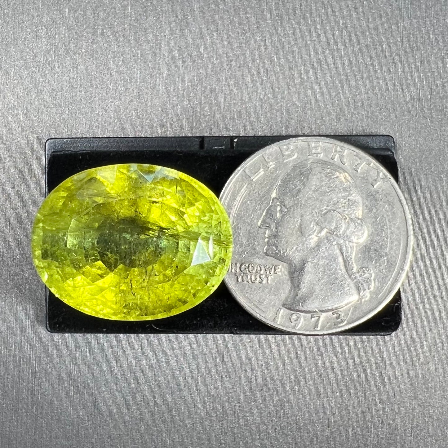 A loose, faceted oval cut green tourmaline stone.  The color is an almost neon yellow-green.