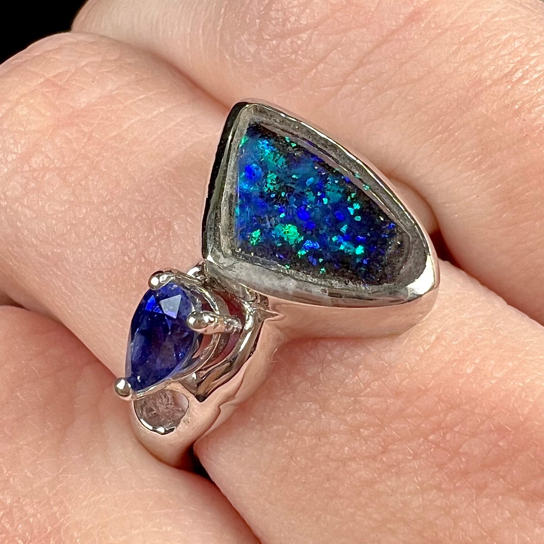 A ladies' white gold ring set with Australian black boulder opal and pear shape blue sapphire.