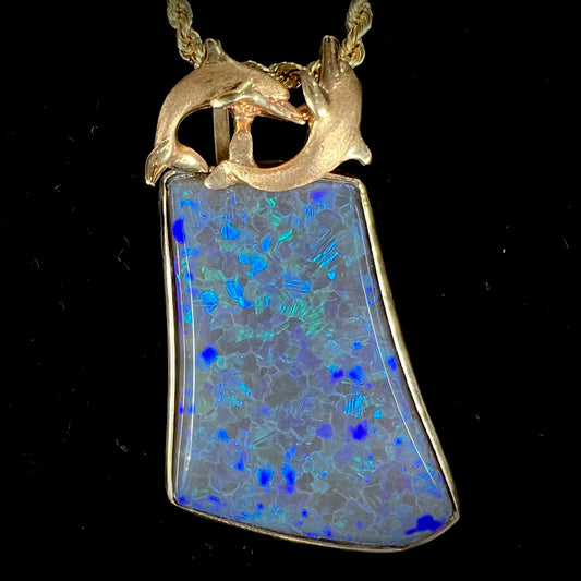 A gold freeform cut black opal bezel pendant cast with two dolphins on top of the opal.