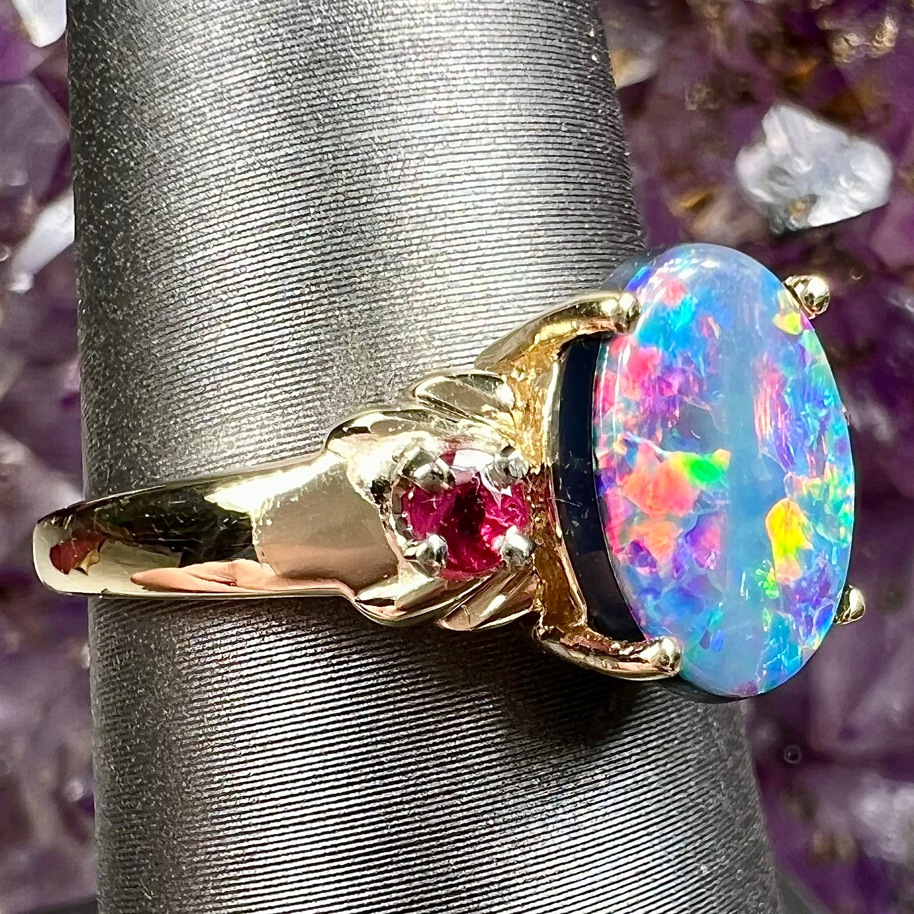 A yellow gold ring prong set with a black opal doublet cabochon and two round ruby accents.