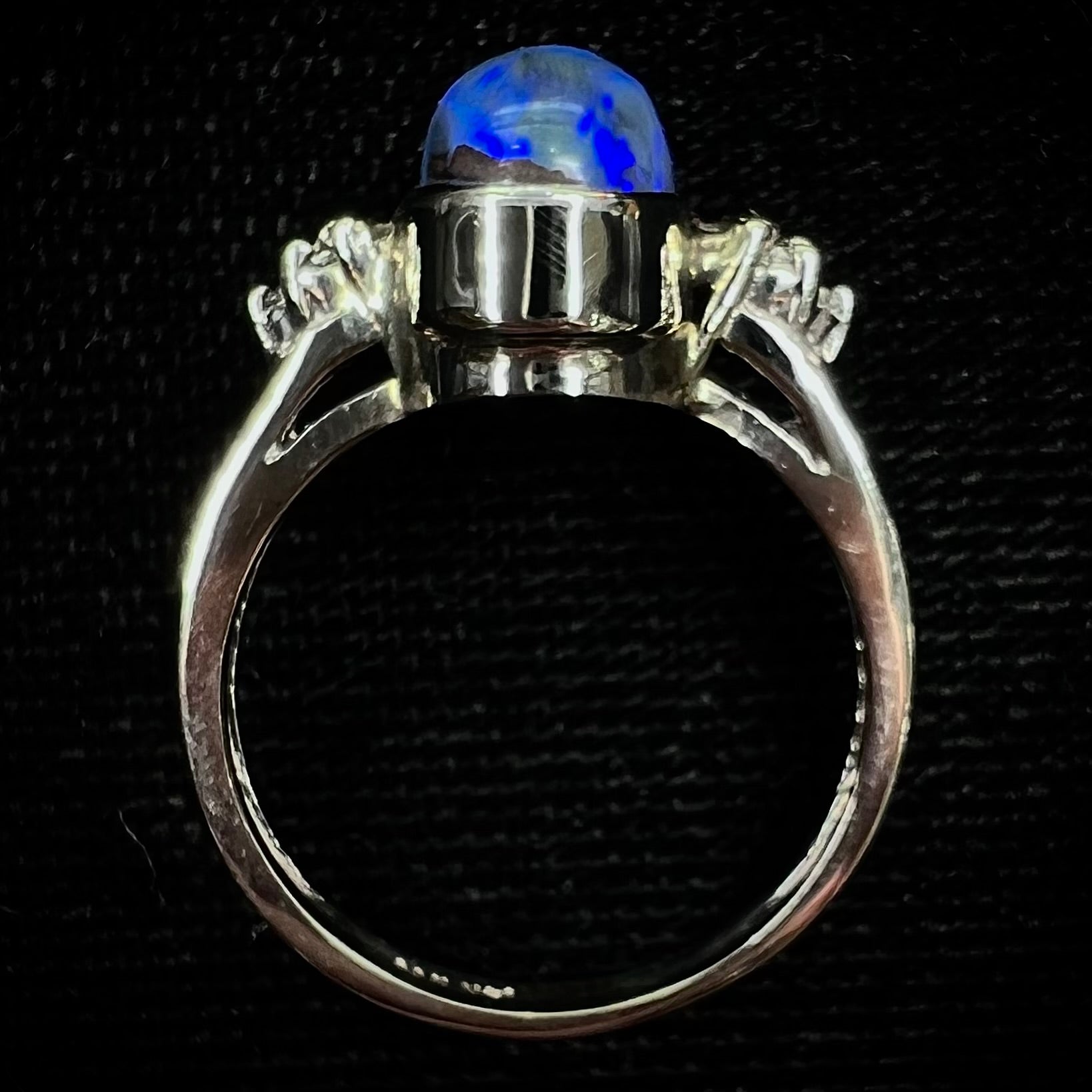 A white gold ring set with a Lightning Ridge black opal and diamond accents.  The opal displays a cat's eye pattern.