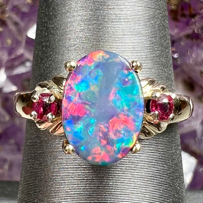 A yellow gold ring prong set with a black opal doublet cabochon and two round ruby accents.