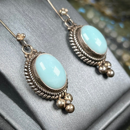 A pair of silver wire dangle earrings set with blue agate stones.  The earrings have a braided rope design.