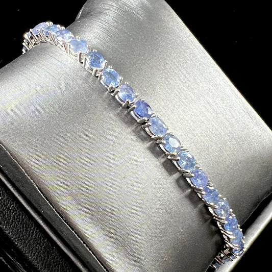 A sterling silver tennis bracelet set with faceted oval cut blue sapphires.