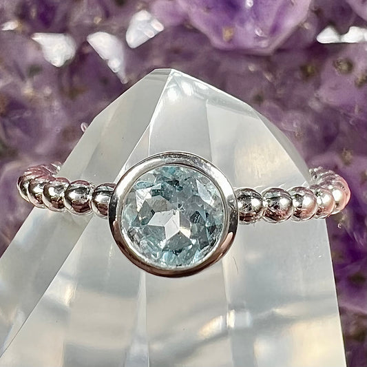 A silver, bezel set, round cut sky blue topaz solitaire ring.  The band is made of connected silver balls.