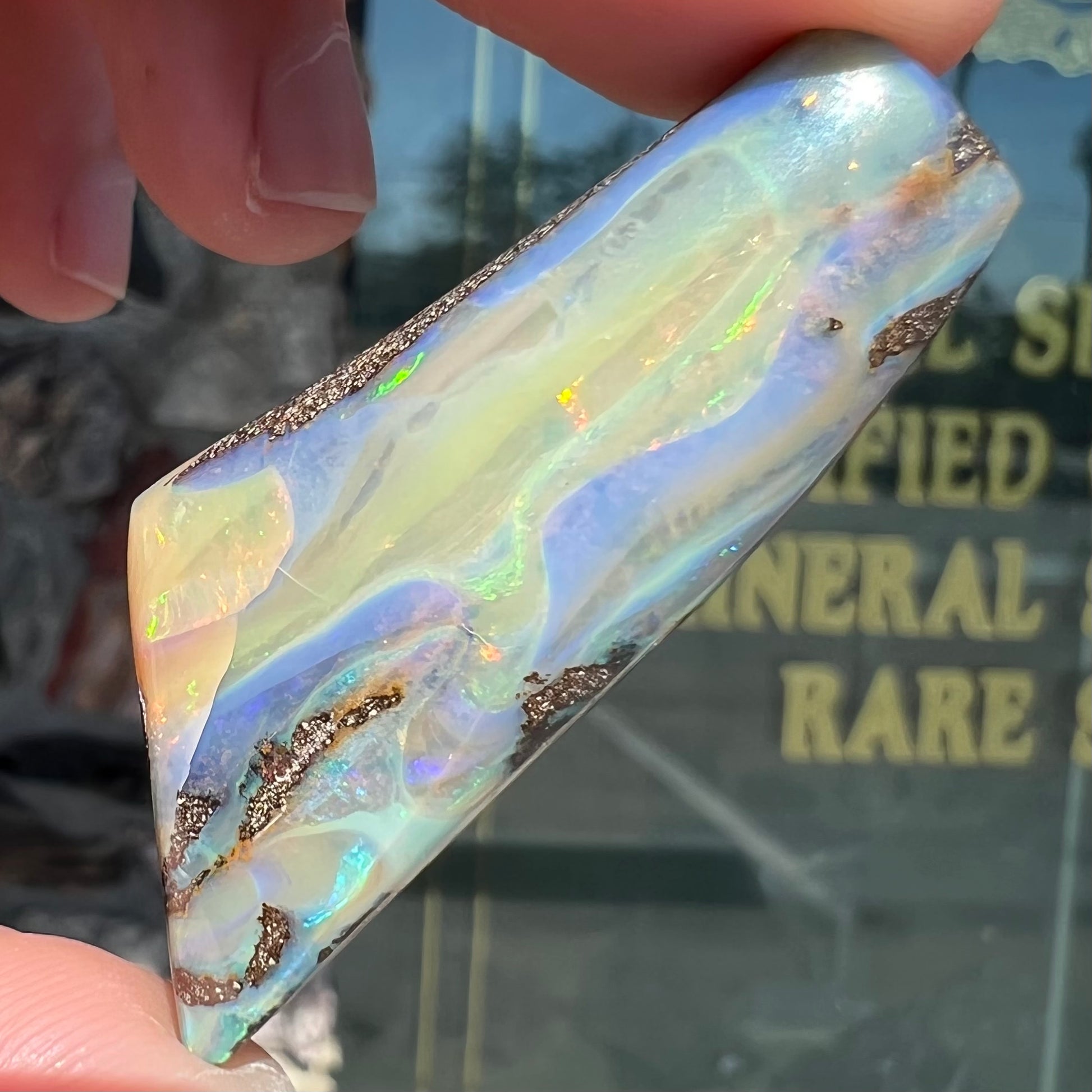 A freeform shaped, polished boulder opal stone from Queensland, Australia.  The stone has red, orange, green, and blue fire.