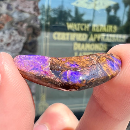 A loose boomerang shaped purple boulder opal stone from Quilpie, Australia.