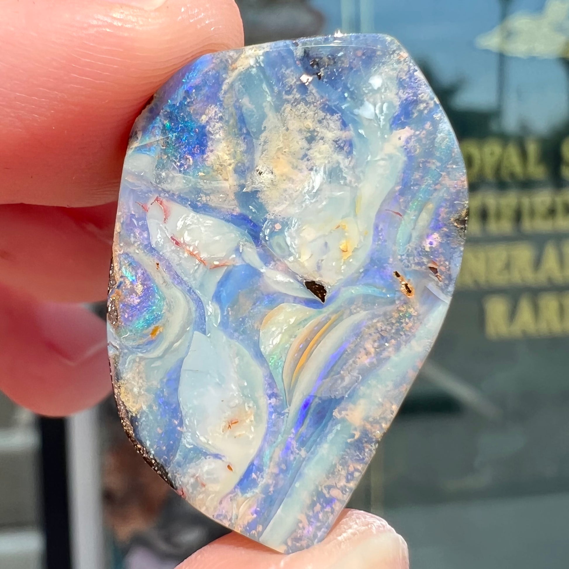 A loose, polished, freeform cut boulder opal stone from Queensland, Australia.