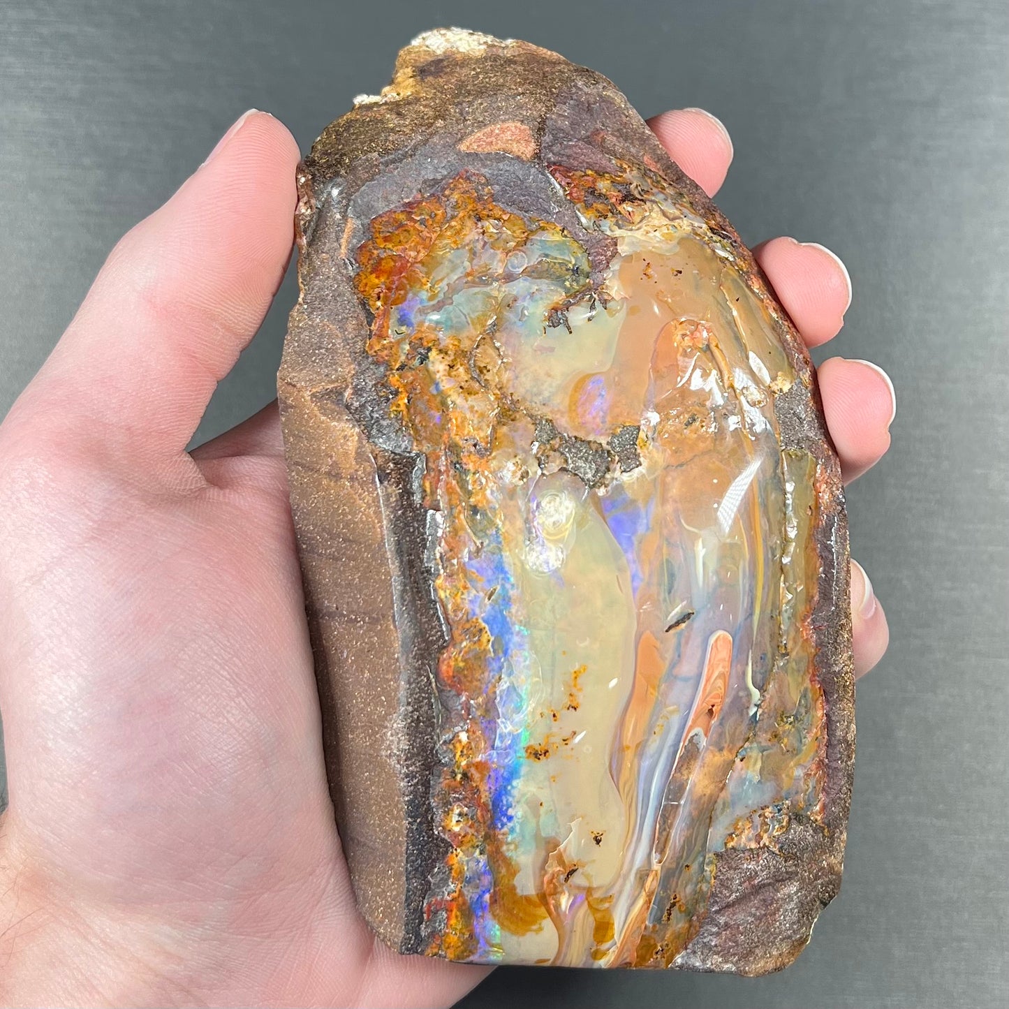 A polished Quilpie boulder opal specimen.  The stone has a stripe of bright blue, green, and purple.