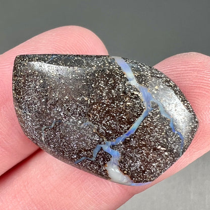 A loose, polished, freeform cut boulder opal stone from Queensland, Australia.