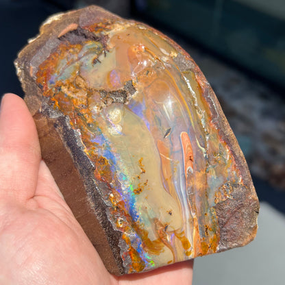 A polished Quilpie boulder opal specimen.  The stone has a stripe of bright blue, green, and purple.